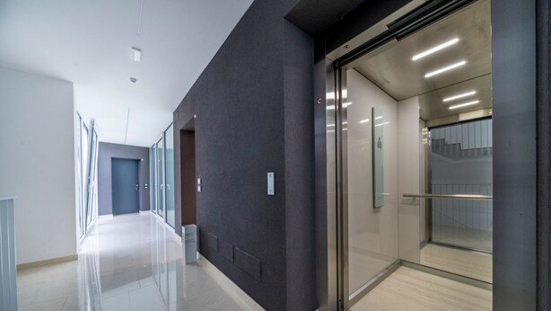 Un pasillo moderno con puertas de cristal, suelo transparente y pared de color claro.