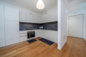 Uma cozinha moderna com armários brancos, forno embutido e painel de bancada preto.