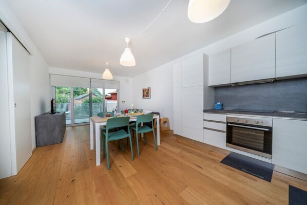 A modern kitchen with white cabinets, a built-in oven, and a dining area with a table and chairs. - GuestHost - Neos House Lovely Apartment (Udine)