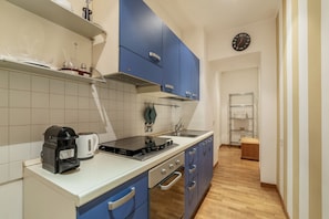 Una cocina compacta con estufa, cafetera y un reloj en la pared.