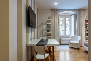 Un comedor con una mesa, sillas, un televisor, una lámpara y una ventana con cortinas.