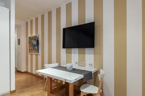 Ein Zimmer mit einem weißen Tisch, zwei Stühlen, einem an der Wand montierten Fernseher und einem Gemälde an der Wand.