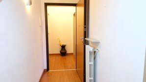 Een gang met een houten vloer, een deur die naar een kamer leidt, een radiator en een wandlamp.