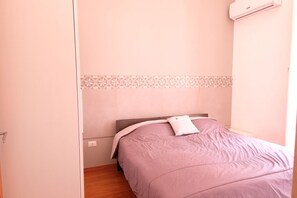 A bedroom with a bed, a wall-mounted air conditioner, and a patterned border on the wall.