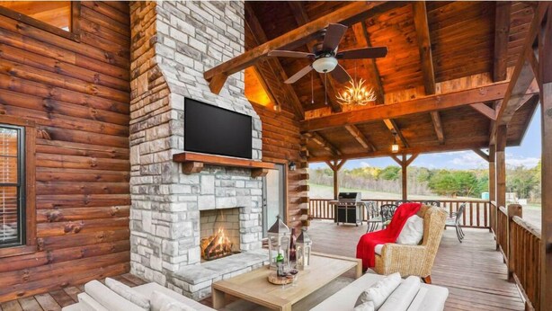 A log cabin with a stone fireplace, outdoor seating, and a patio area. - The Burrow Lodge! Pet Friendly! Hot Tub! Sleeps 16 (Logan)