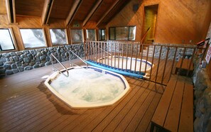 A hot tub in a wooden cabin with stone walls and large windows.