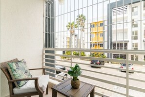 Enjoy the view from this balcony with a wicker chair, cushion, and small table.