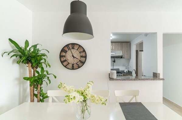 Enjoy a meal for two in this stylish dining area with a clean table setting, a statement clock, and a touch of greenery.
