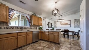 A kitchen with wooden cabinets, a dishwasher, a dining area with a table and chairs, and a hanging light fixture. - Brand New! Restoration Retreat (Flagstaff)