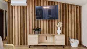 Un salon moderne avec un mur composé de lambris en bois, un téléviseur à écran plat fixé au-dessus d’un meuble en bois, et une plante en pot posée sur le meuble.