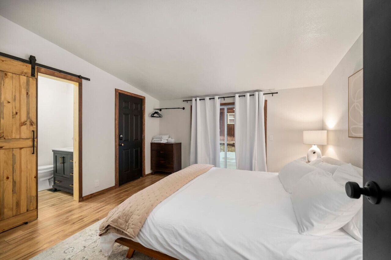 Un dormitorio con una cama, un armario de madera, una puerta y una ventana con cortinas.