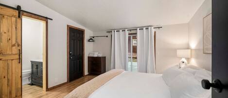 Un dormitorio con una cama, un armario de madera, una puerta y una ventana con cortinas.