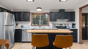 Une cuisine moderne avec des meubles de couleur sombre, des appareils en acier inoxydable et un îlot central doté de deux chaises.