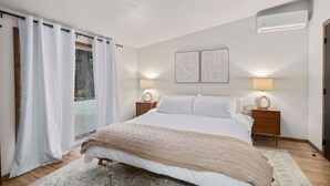 Une chambre dotée d’un grand lit, de deux tables de chevet avec des lampes, d’une vue sur l’extérieur et d’un climatiseur fixé au plafond.