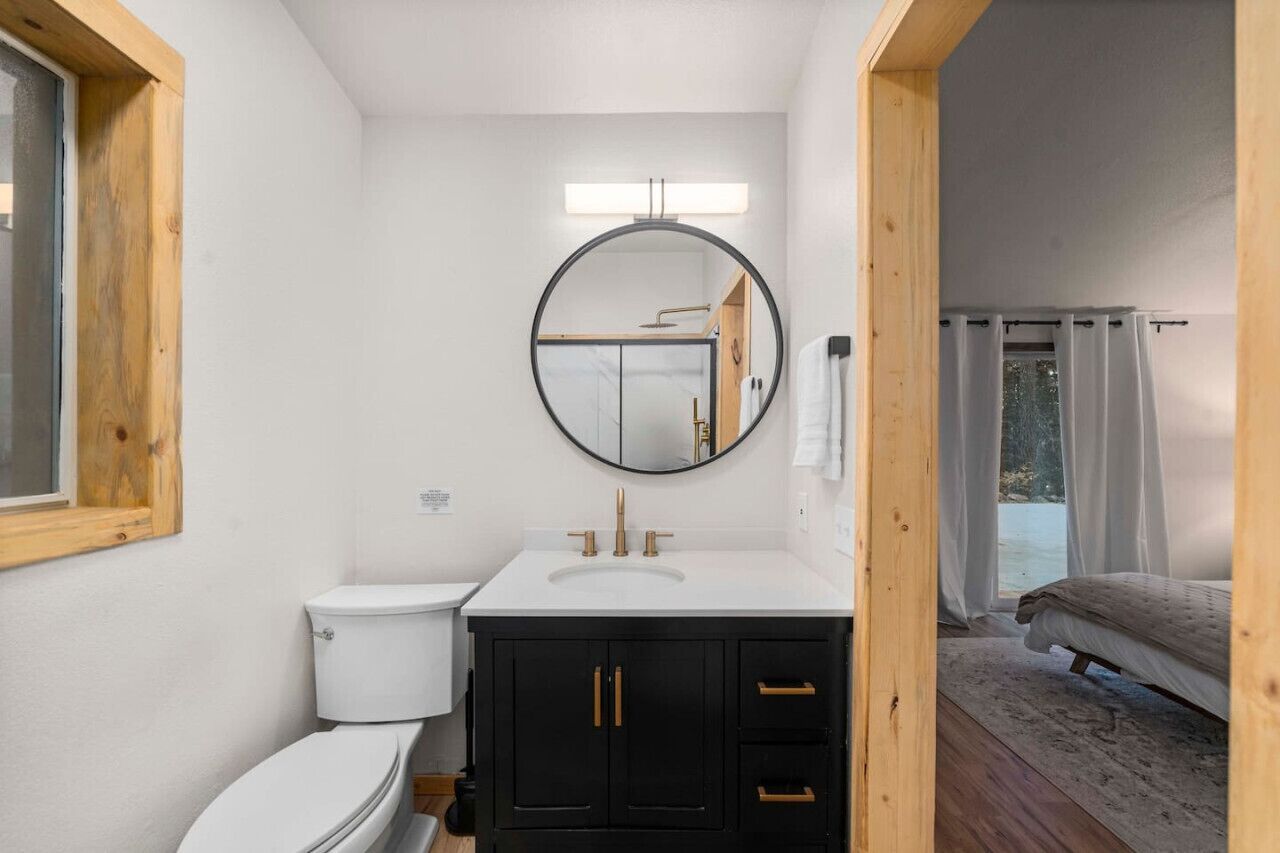 A bathroom with a white toilet, a black vanity with gold handles, and a round mirror above the sink.