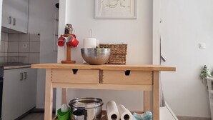 Et køkken med et træbord der holder køkkenudstyr, billedkunst på væggen og udsigt til det tilstødende opholdsstue.