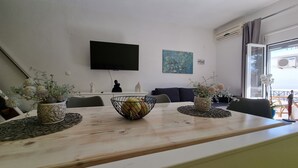 En moderne stue med spisebord, stole, et fladskærms-tv, dekorative vaser og et stort vindue med udsigt.