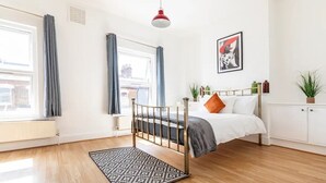 Une chambre à coucher avec un lit, une fenêtre avec des rideaux, un radiateur, une lampe suspendue et une plante.