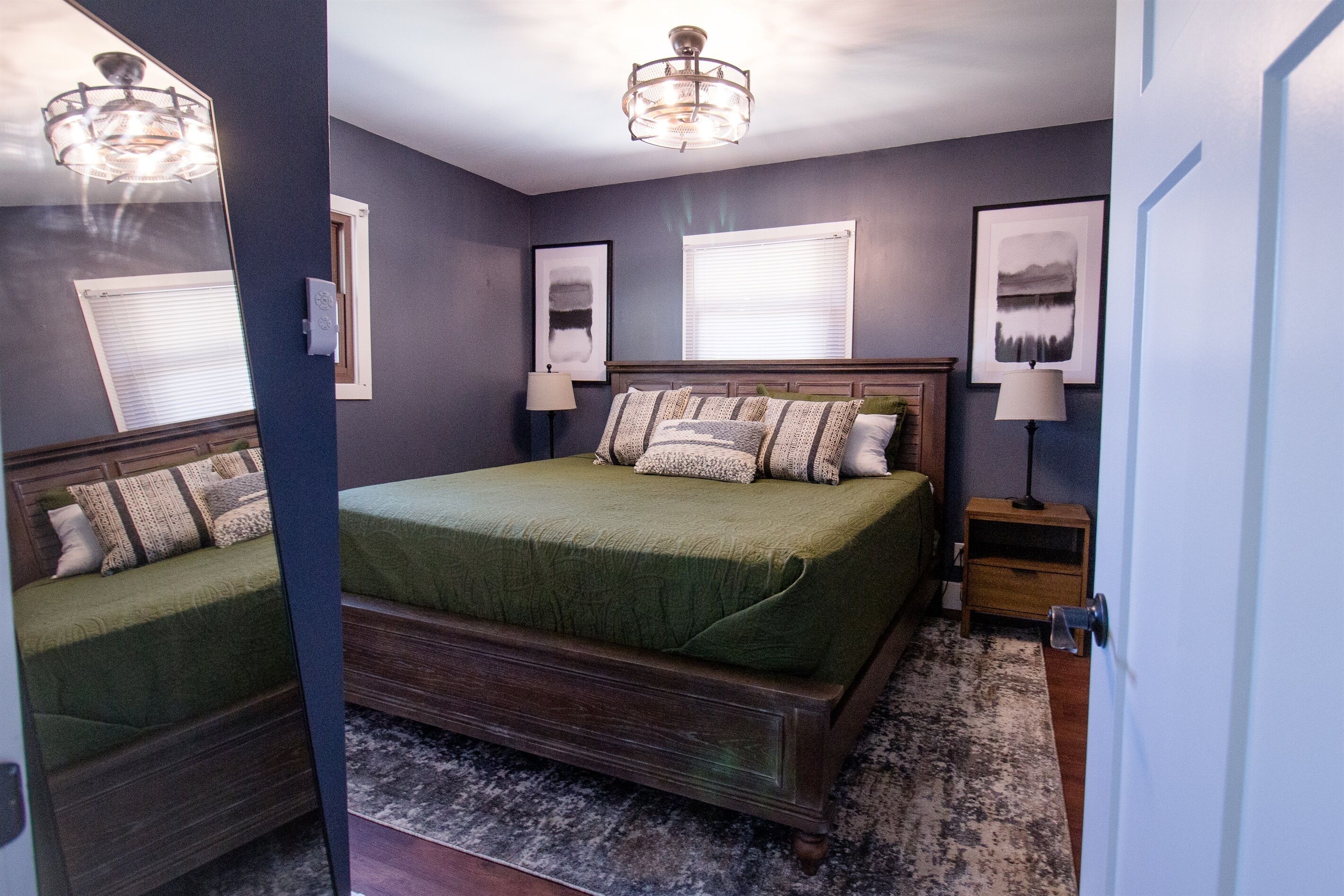 Une chambre à coucher avec un grand lit, deux tables de chevet, une commode, un lustre et des œuvres d’art encadrées accrochées aux murs.