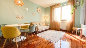 A cozy living room with a wooden floor, a round dining table with chairs, a sofa, and a large window with curtains. - GIALLOMANGO Apt in Lucca (Lucca)