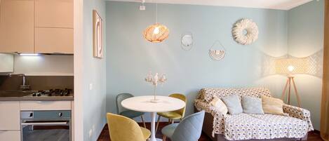 Une cuisine moderne équipée d’une cuisinière à gaz, un coin repas avec une table ronde et des chaises, un canapé agrémenté de coussins à motifs et un lampadaire.