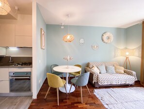 A modern kitchen with a gas stove, a dining area with a round table and chairs, a sofa with patterned cushions, and a floor lamp. - GIALLOMANGO Apt in Lucca (Lucca)