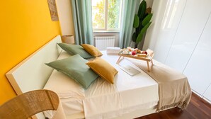 A neatly made bed with pillows, a tray with breakfast items, and a laptop on a white bedspread. - GIALLOMANGO Apt in Lucca (Lucca)