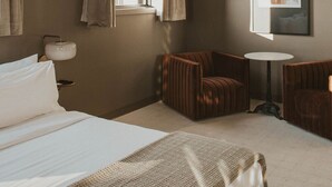 A hotel room with a large bed, a small round table, two armchairs, a wall-mounted lamp, and a framed picture. - Luxury Suite Downtown Berlin 302 (Millersburg)
