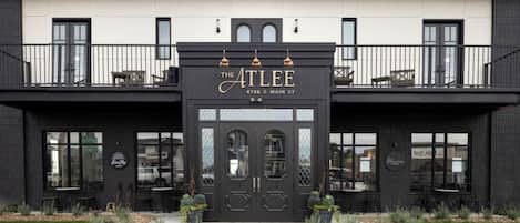 A building with a black facade, a sign reading 'The Atlee 4786 E Main St', and a balcony with seating.