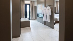 Une chambre d’hôtel dotée d’une grande porte en arc donnant sur une chambre à coucher, une baignoire et un lit recouvert de draps blancs.
