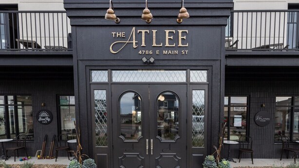 L’extérieur du bâtiment Atlee, un édifice moderne à la façade sombre, est doté de deux grandes portes en arc de cercle et d’une enseigne au-dessus de l’entrée.