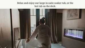 Eine Person in weißer Kleidung steht neben einer großzügigen Badewanne mit Stadtblick.