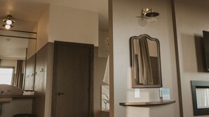 Ein Hotelzimmer mit Essbereich, einem großen Spiegel, einem Fernseher und einer Tür zu einem weiteren Raum.