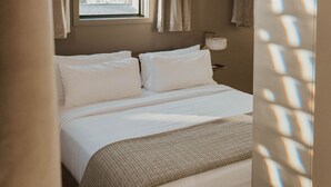 A hotel room with a bed, curtains, a window, and a lamp.