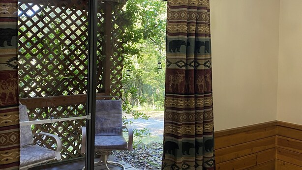 Een kamer met een schuifglazen deur die uitkomt op een terras met stoelen en een houten bank.