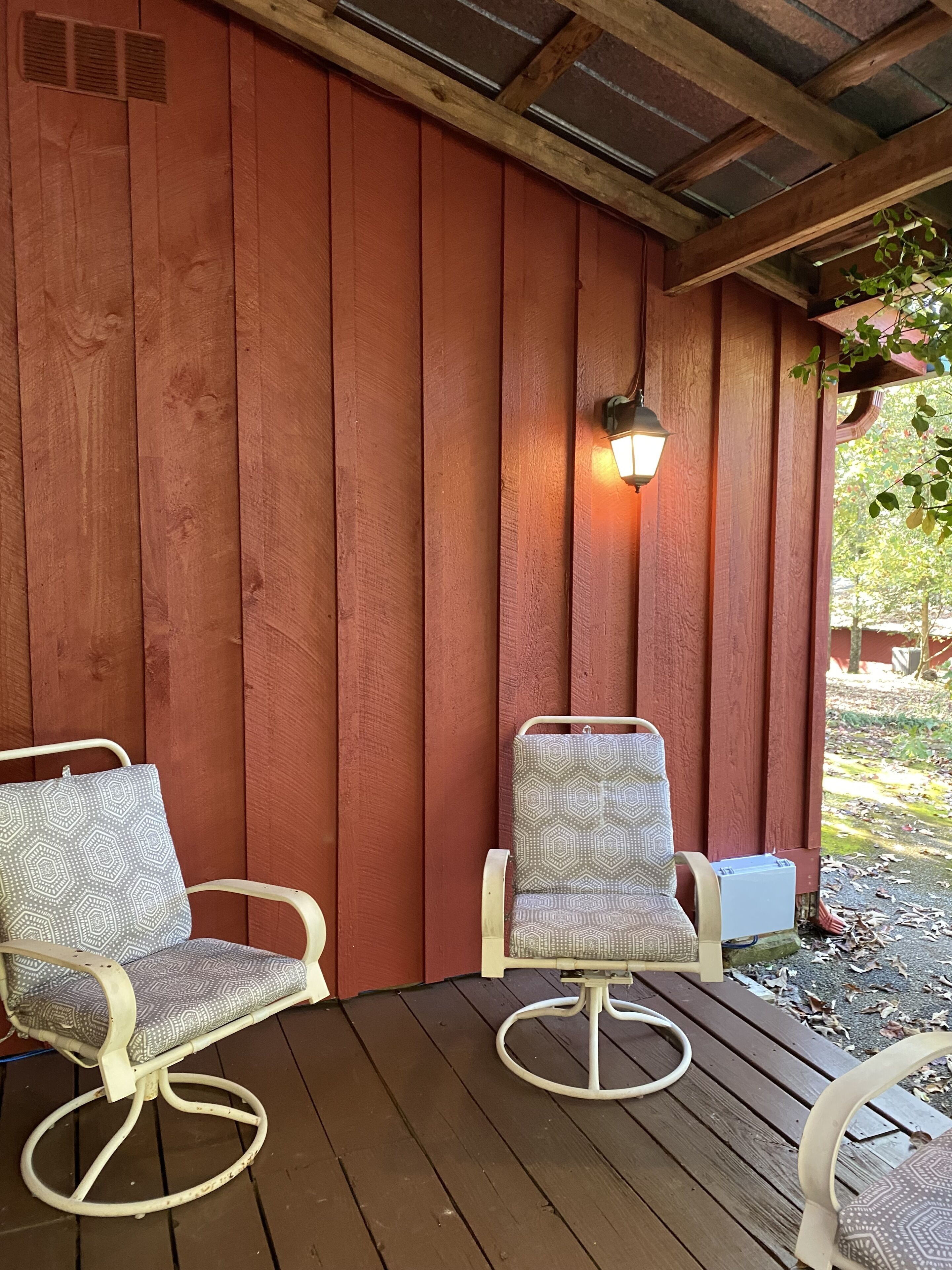 Una terraza de madera con dos sillas y una lámpara fijada a la pared.