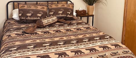 Un dormitorio con una cama con colcha estampada, un cuadro de paisaje enmarco, un letrero motivacional y una planta en maceta.