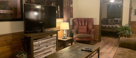 A living room with a television, a red armchair, a sofa, a coffee table, and a lamp.