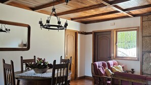 A dining area with a wooden table and chairs, a chandelier, and a window with a view of greenery. - Casa das Acácias (Cabeceiras de Basto)