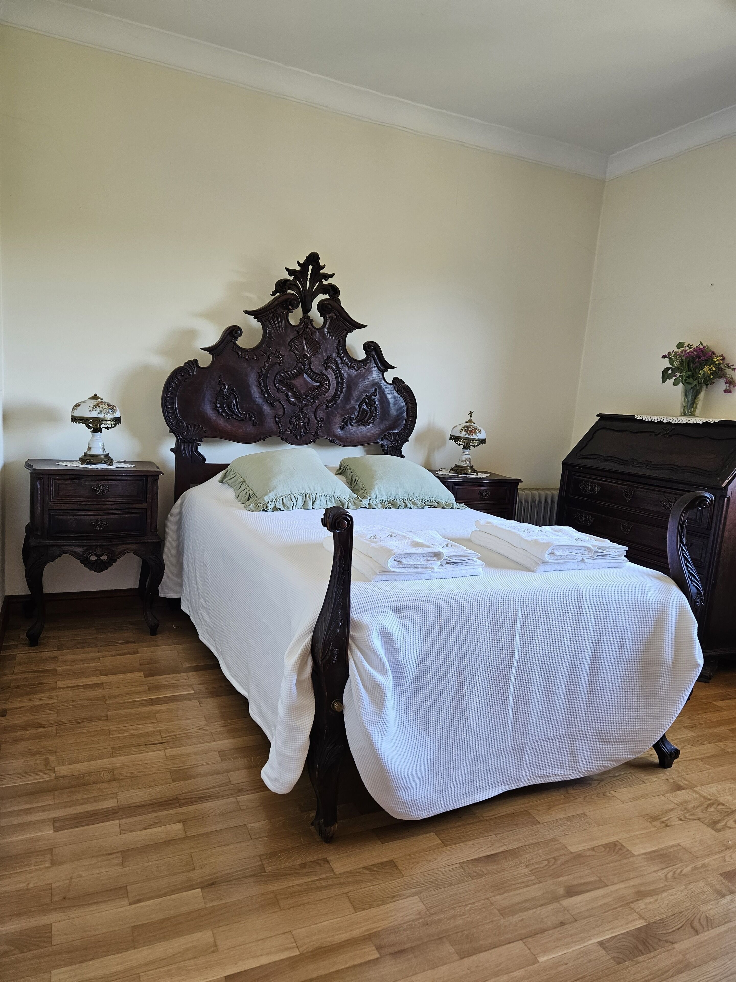 A bedroom with a large bed, two nightstands, a dresser, and a vase with flowers on the dresser.