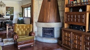 A traditional living room with a fireplace, leather armchair, wooden bookshelves, and a patterned rug. - Casa das Acácias (Cabeceiras de Basto)