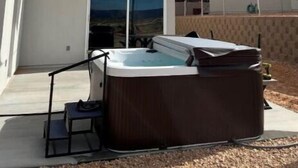 Een moderne buitenruimte met een jacuzzi, een overdekte zithoek en een groot zonnescherm.