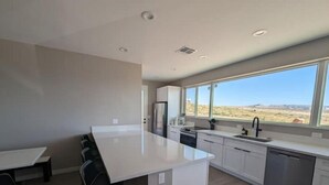 Een moderne keuken met een groot eiland, witte kastjes en uitzicht op een woestijnlandschap door grote ramen.