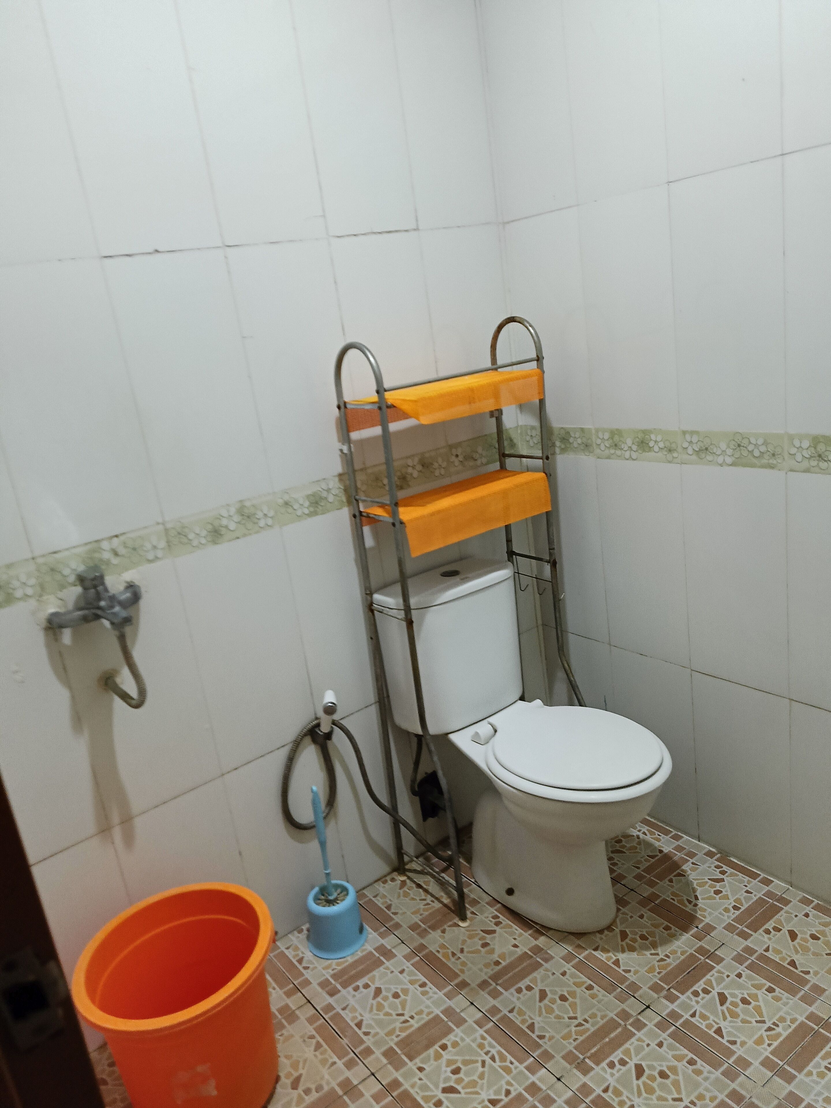 A bathroom with a toilet, a metal shelf, a shower, and a mop bucket.