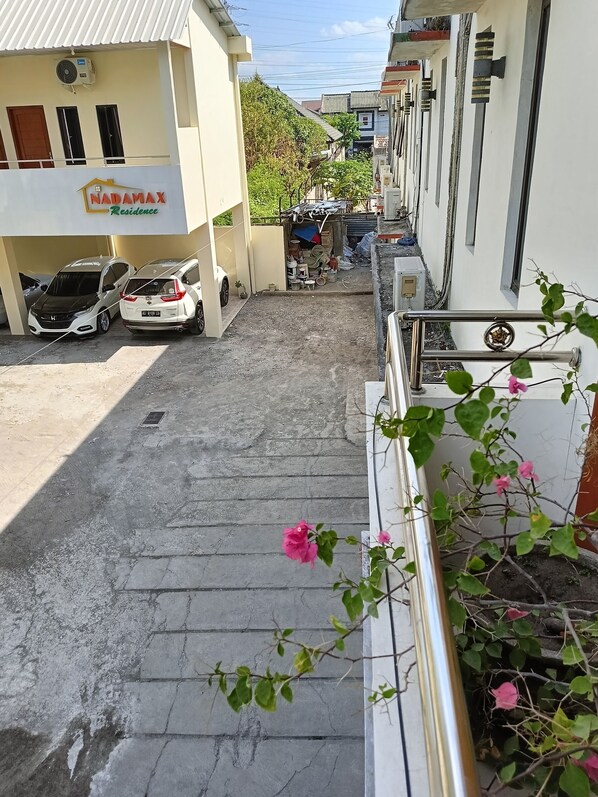 A residential area with a building labeled 'NADAMAX Residence'. There are parked cars, a small shop, and a staircase leading to a balcony with a railing.