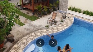 Ein Swimmingpool mit gefliestem Deck, einem Pavillon und Topfpflanzen.