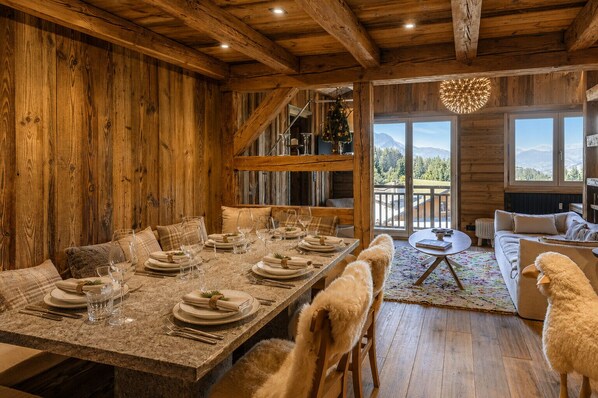 A rustic dining area with a wooden table set for six, a staircase, and a view of the outdoors.