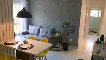 Um espaço de estar moderno com área de jantar, sofá e uma pequena mesa com planta em vaso.