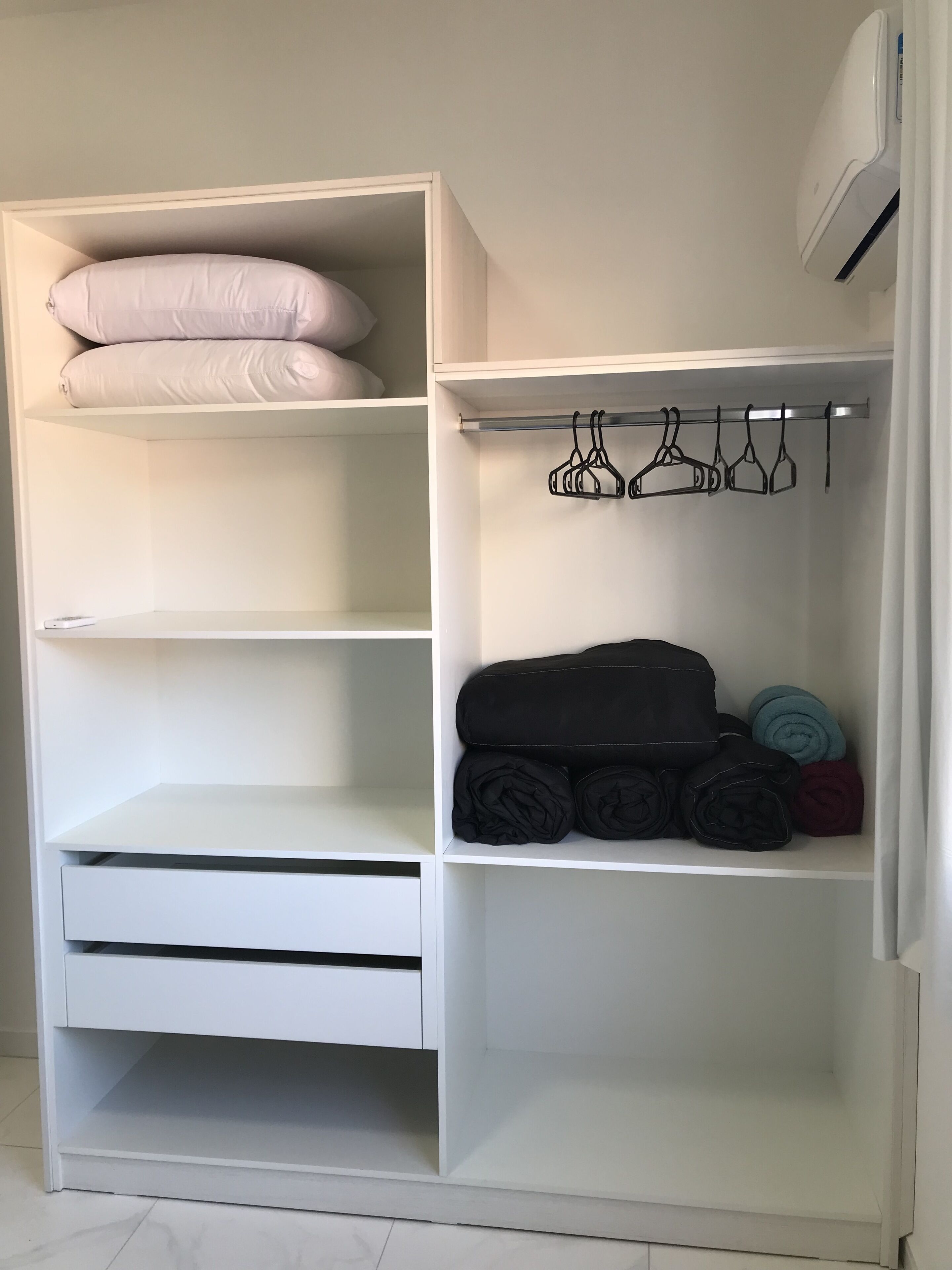 Armário branco com prateleiras, barra para pendurar roupas e espaço para guardar objetos dobrados.