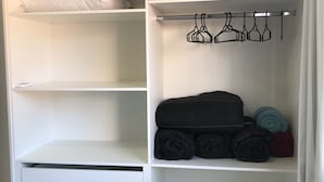 Valkoinen vaatekaappi, jossa on hyllyjä, henkaritanko ja tila, johon voi laittaa taiteltuja vaatteita tai muita tavaroita.